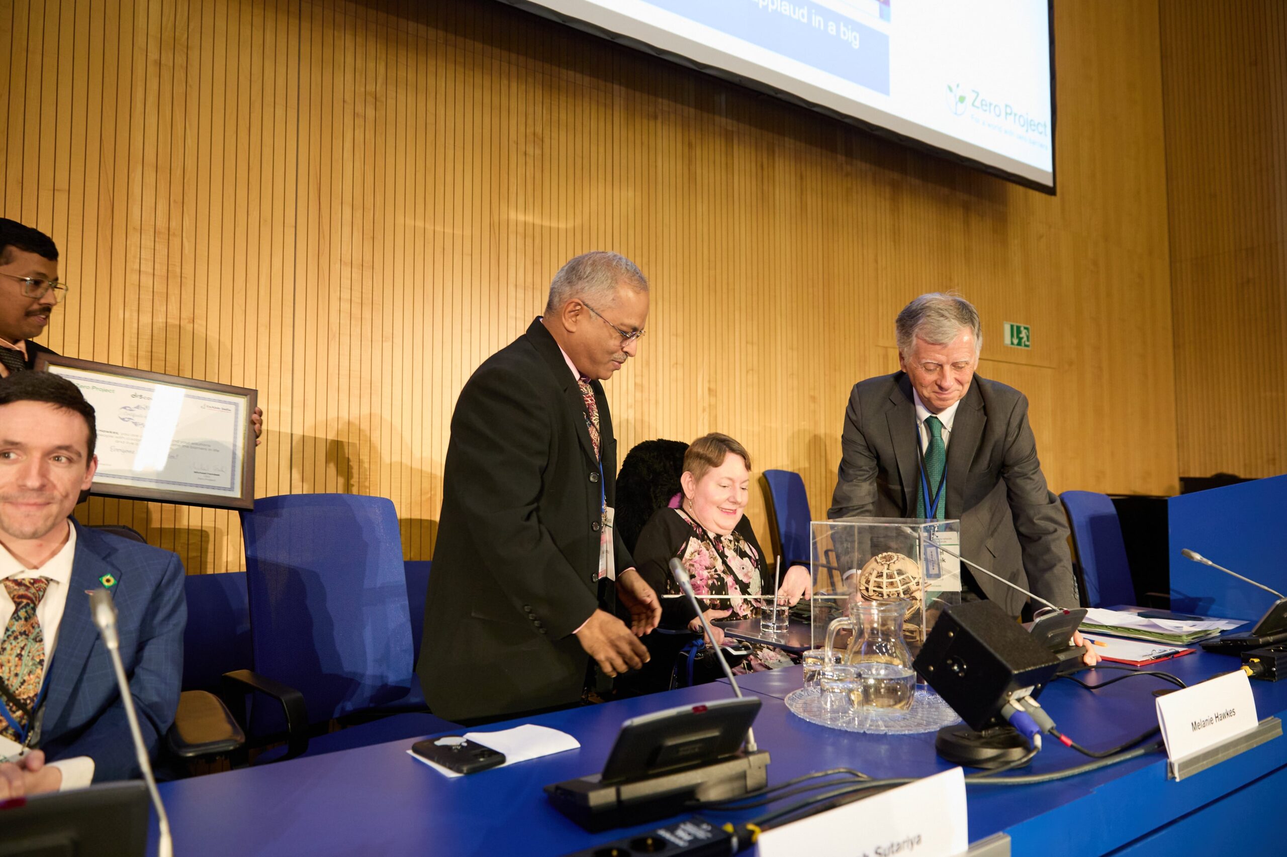 Three individuals, including a woman in a wheelchair, participating in a formal event promoting disability inclusion.