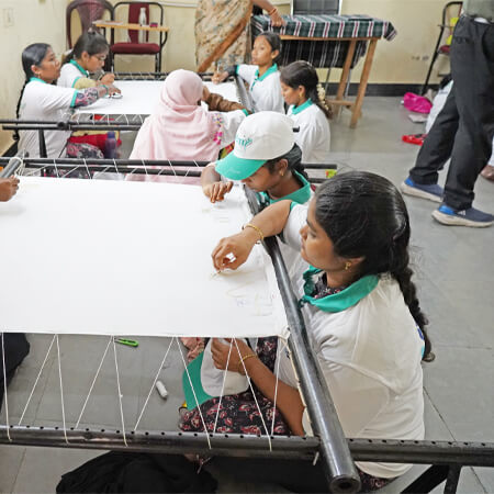 Group of women and girls participating in an embroidery or fabric work training session.
