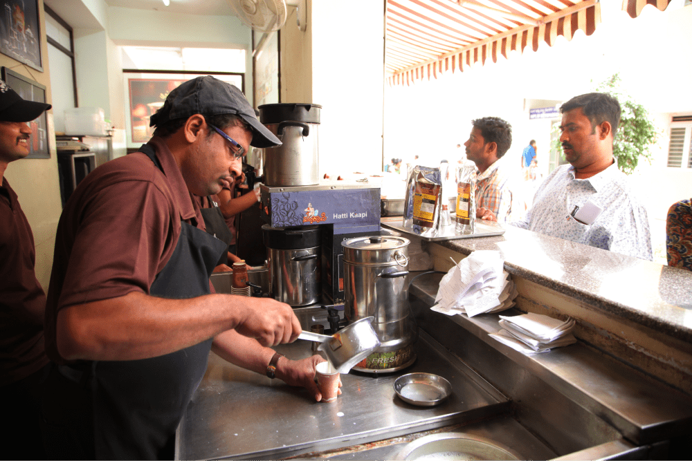 Man preparing coffee at a food stall, representing livelihood initiatives.