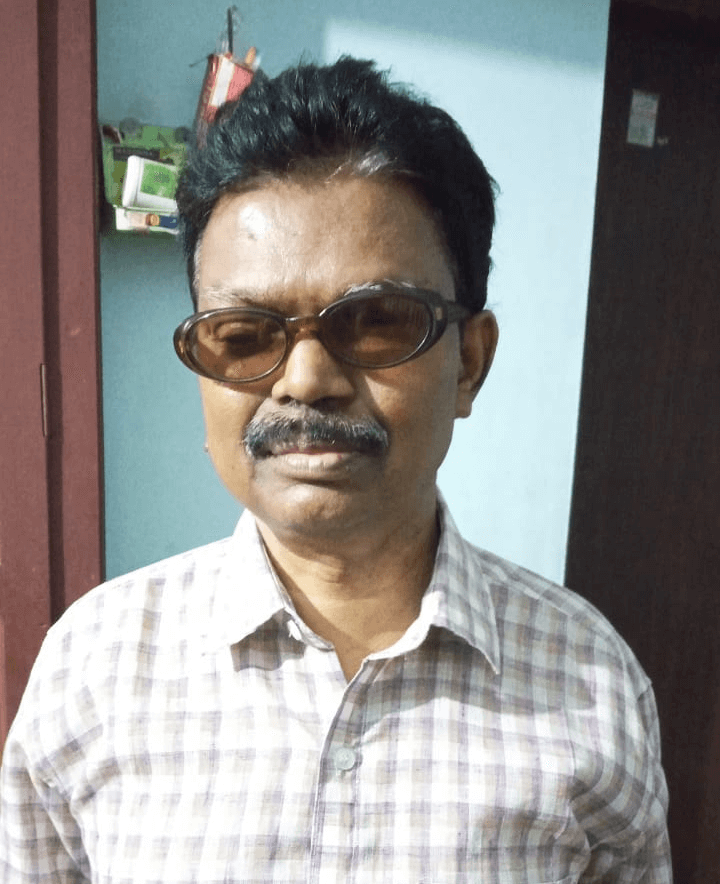 Portrait of a middle-aged man with dark hair and a mustache, wearing tinted glasses and a checked shirt.