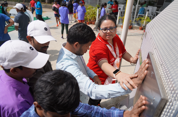Volunteer guiding a group of people, some with disabilities, touching a textured metallic panel outdoors.