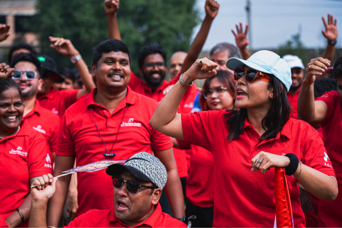 A group of people wearing matching red shirts cheering and raising their hands during an outdoor event.